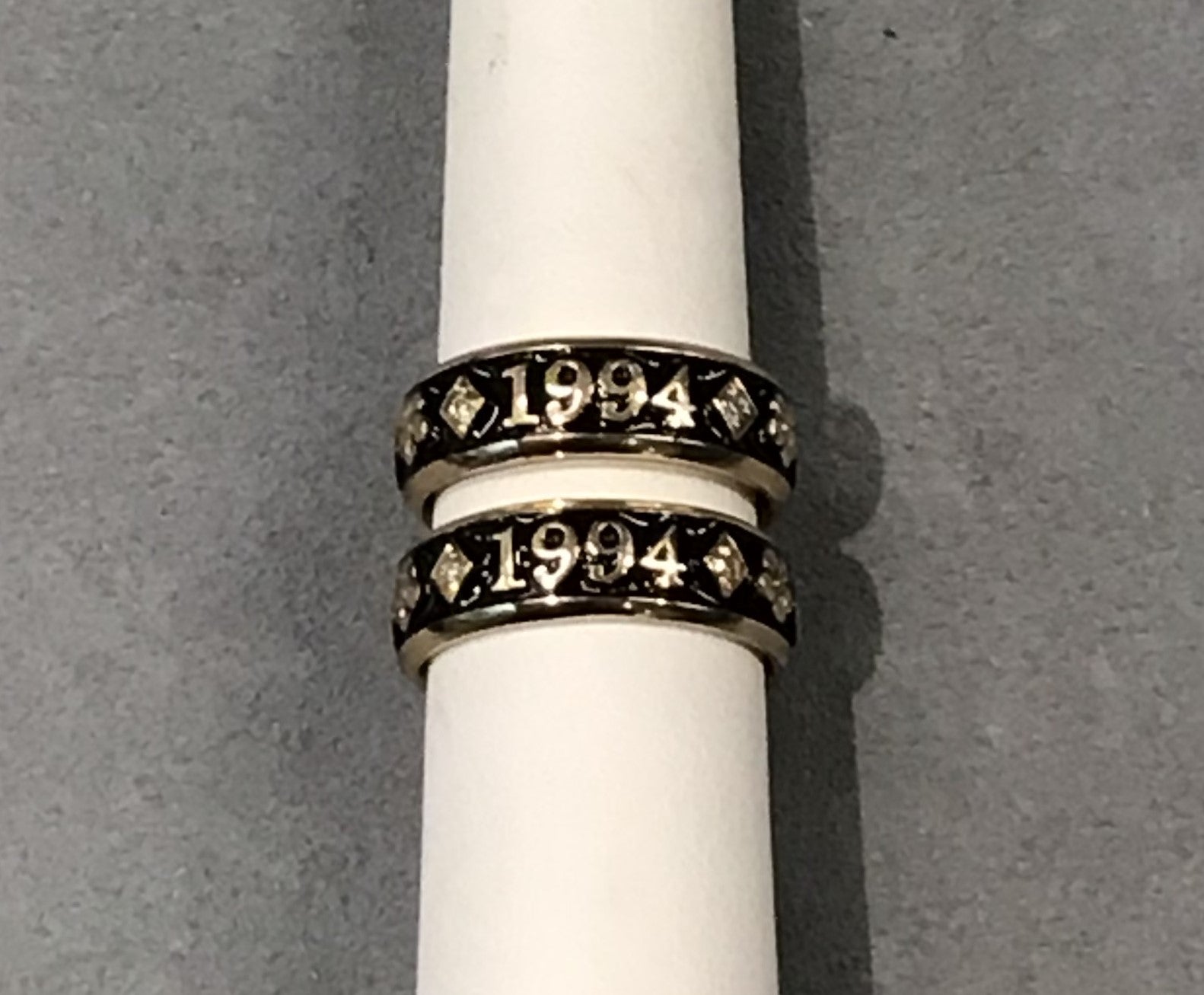 Two bands on a white ring mandrel with a grey background. Rings have the letters 1994 on them. 