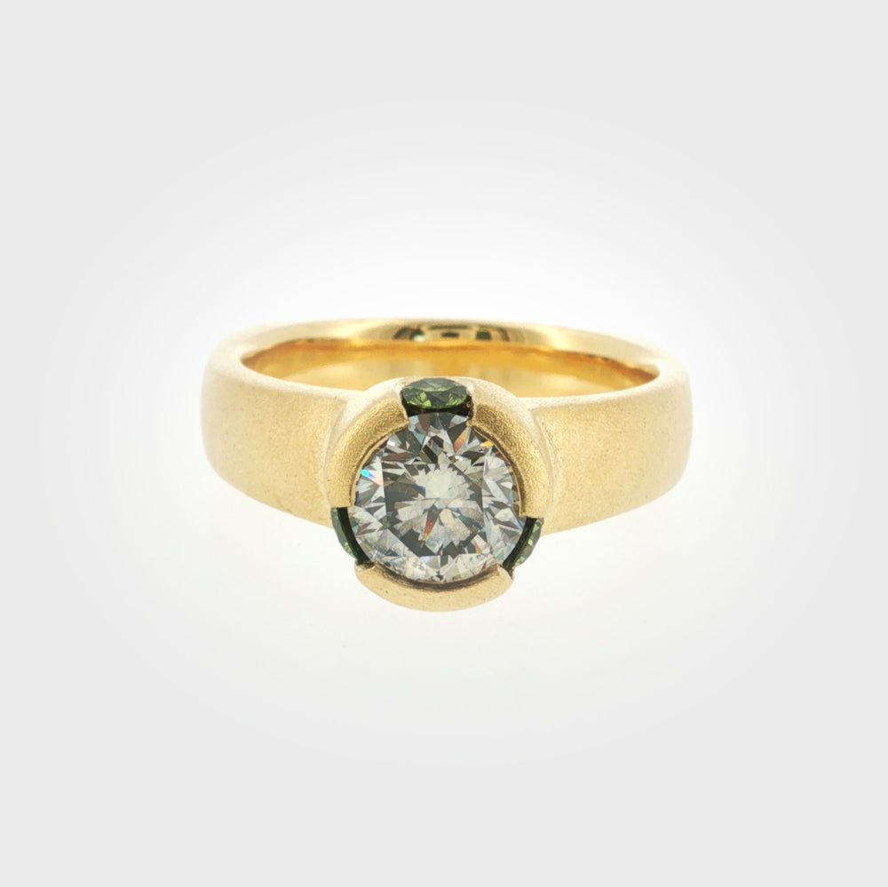 Gold textured ring with center diamond surrounded by three green gemstones, photographed on a white background. 