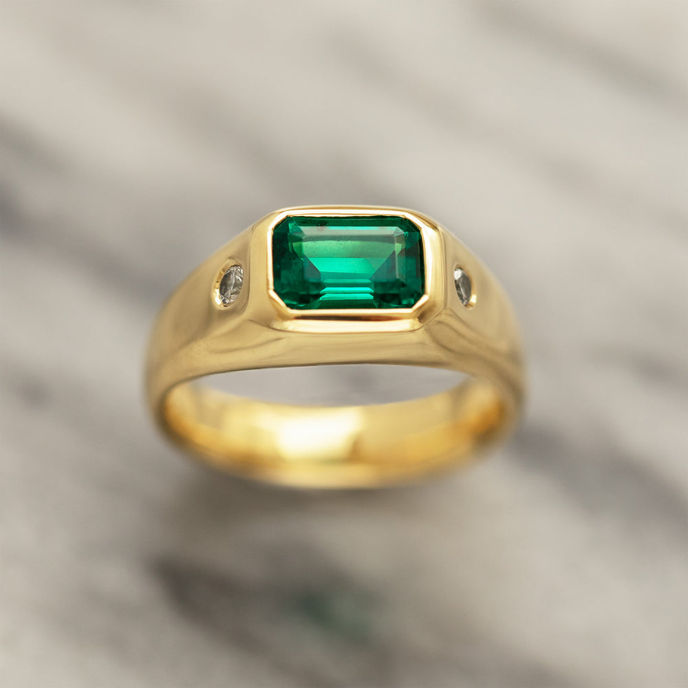 Gold ring with a green gemstone and two side diamonds on a marble background. 