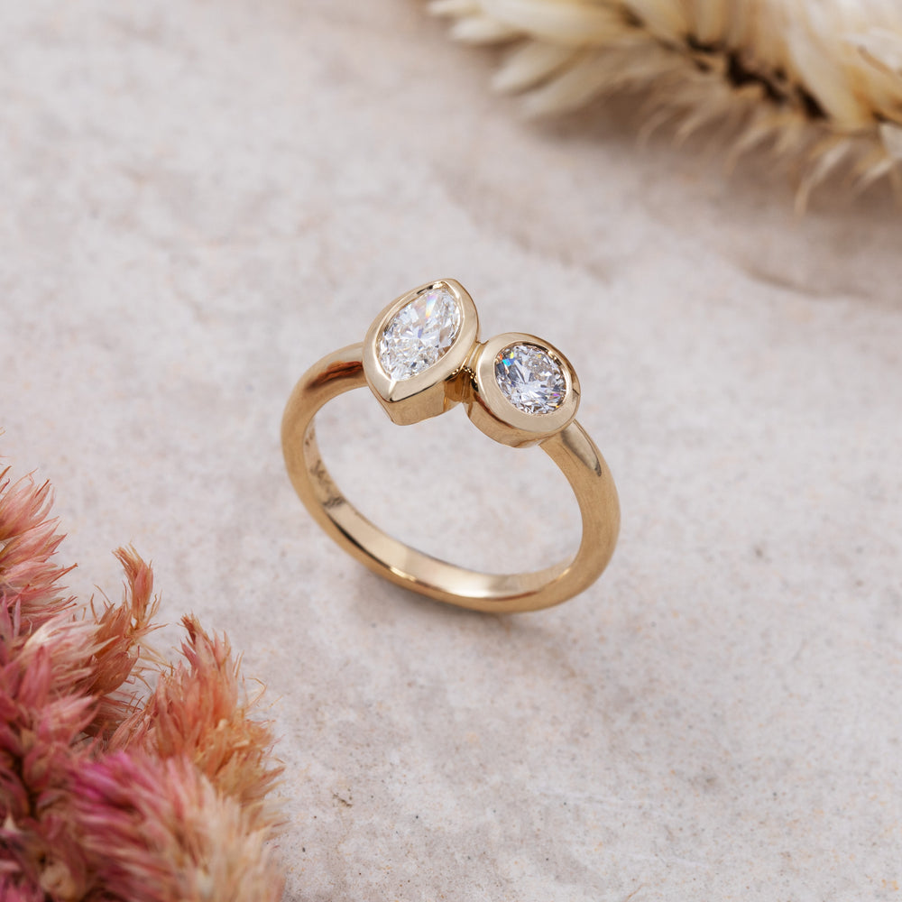 Gold ring with two diamonds on a textured surface with dried flowers