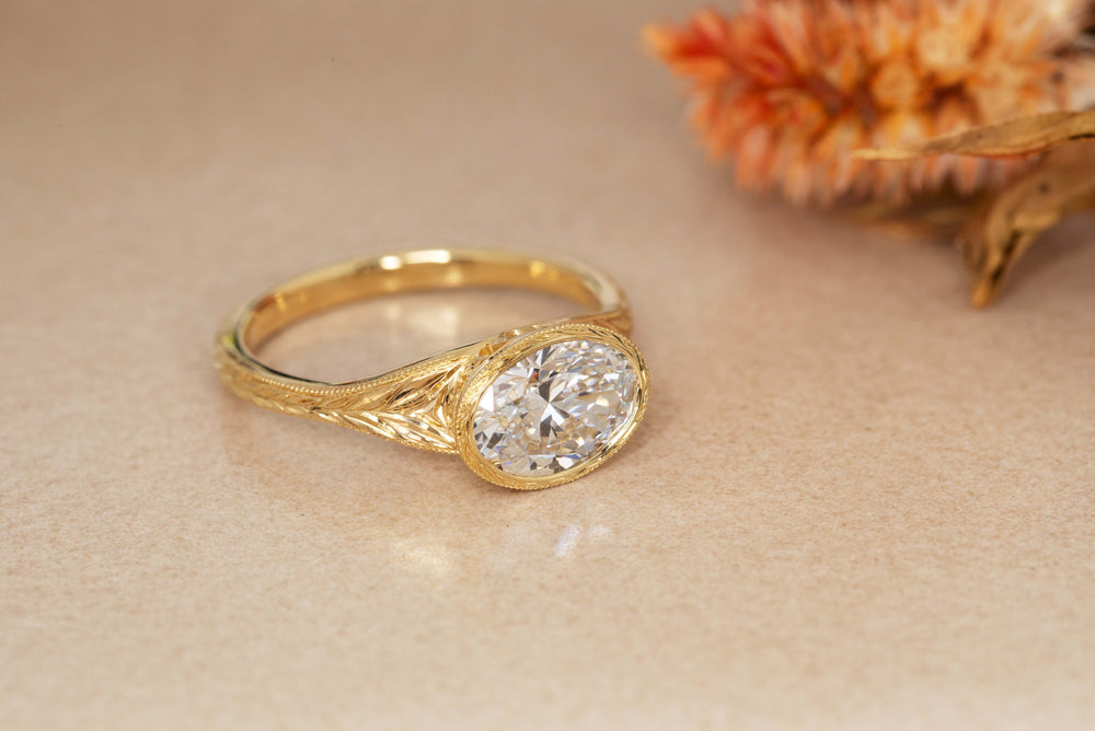 Yellow gold ring featuring bezel set oval cut Diamond on band with hand engraving