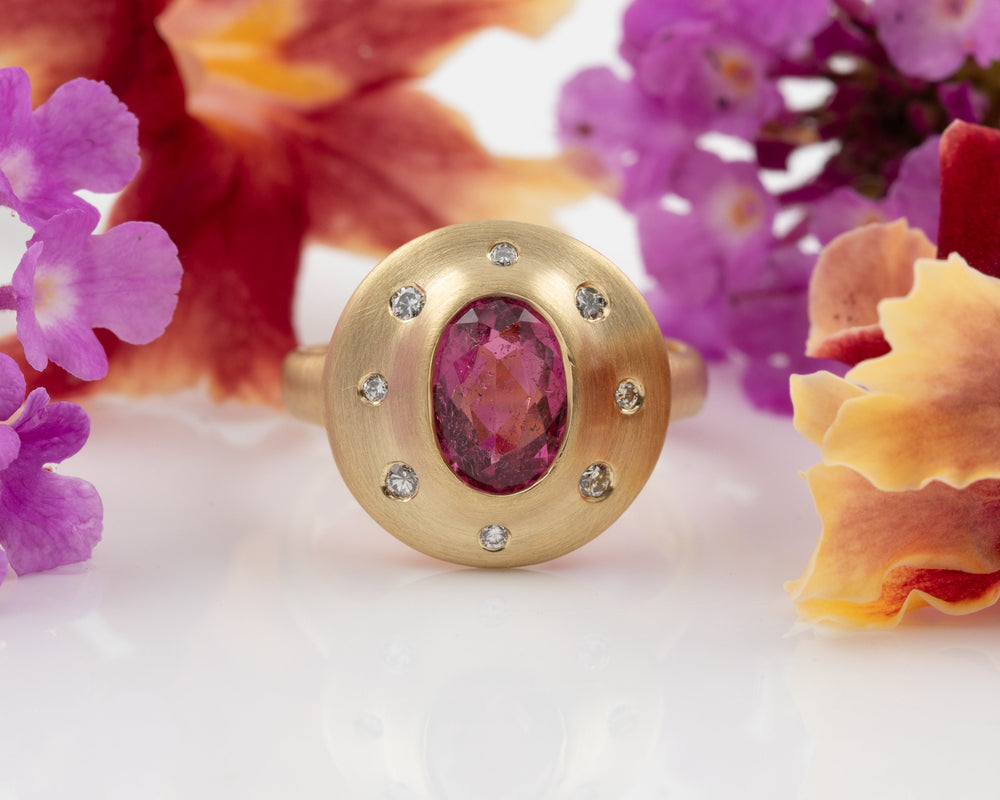 Gold ring with a pink gemstone surrounded by flowers on a white background