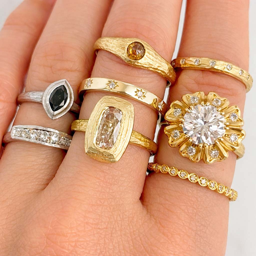 Hand wearing multiple gold and silver toned rings with various designs.