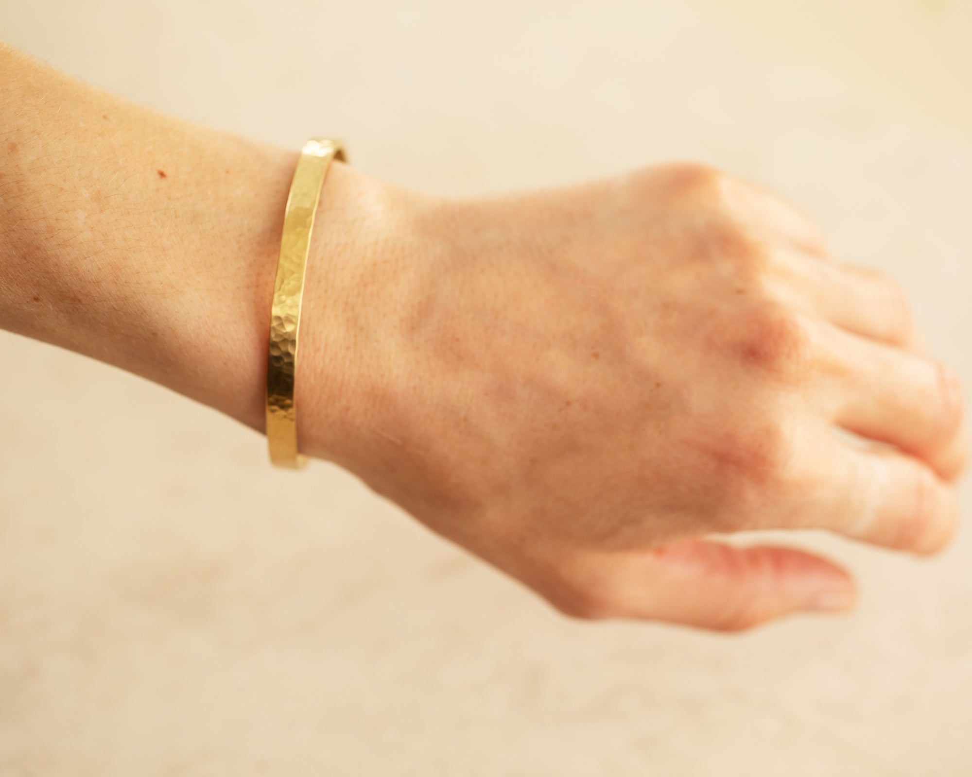 Gold hammer finished bracelet on an arm on a tan background