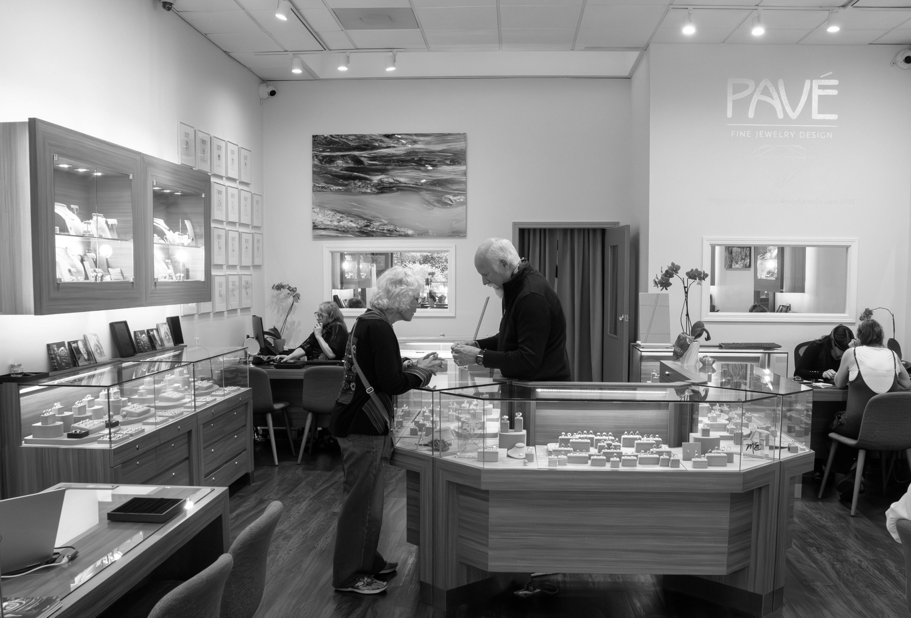 View of the inside of the Pave Fine Jewelry Design store in Oakland California. Founder Michael Endlich is talking with a client in the center, and staff and other clients are at the tables behind jewelry cases. 