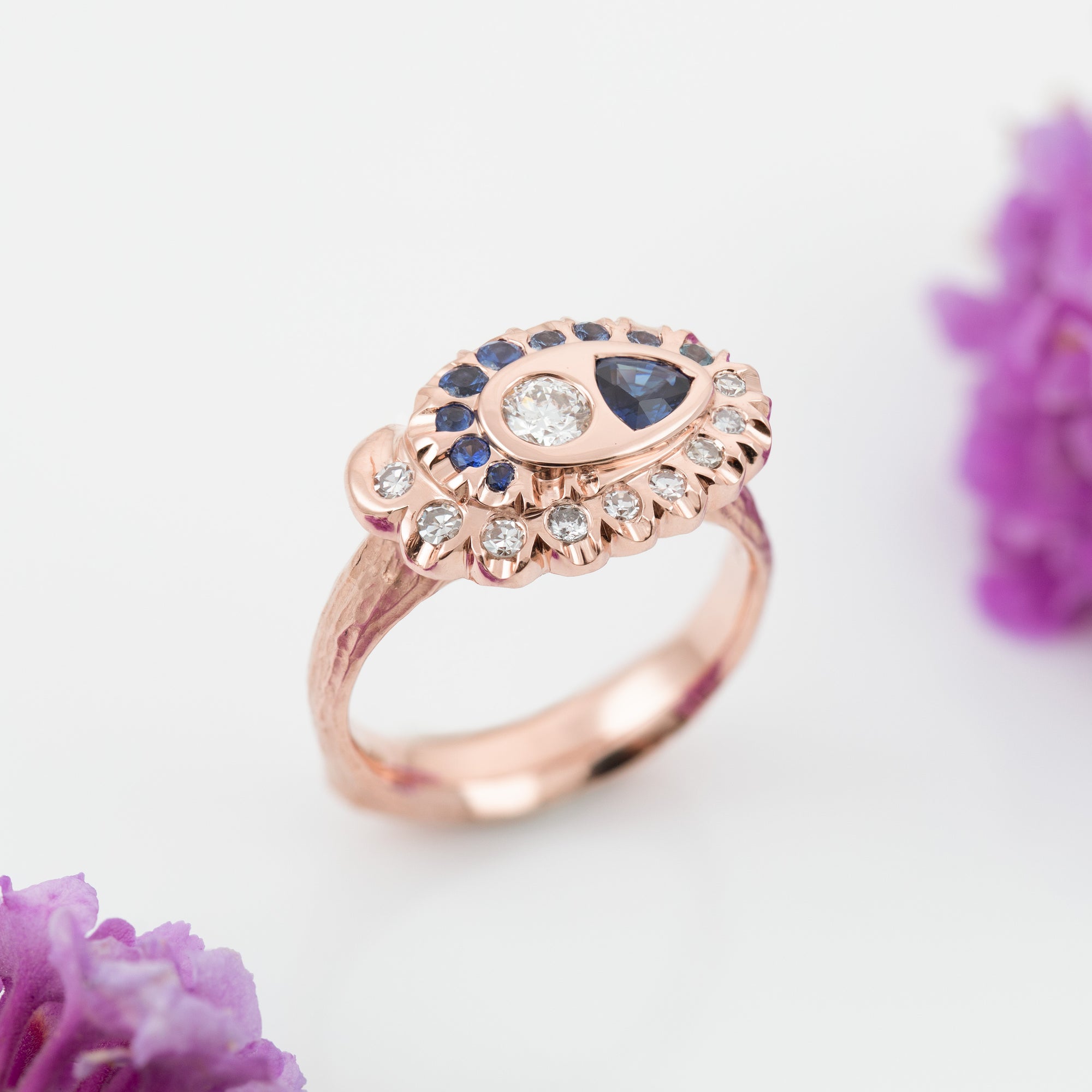 Rose gold ring with a spiral pattern of diamonds and blue gemstones on a white background