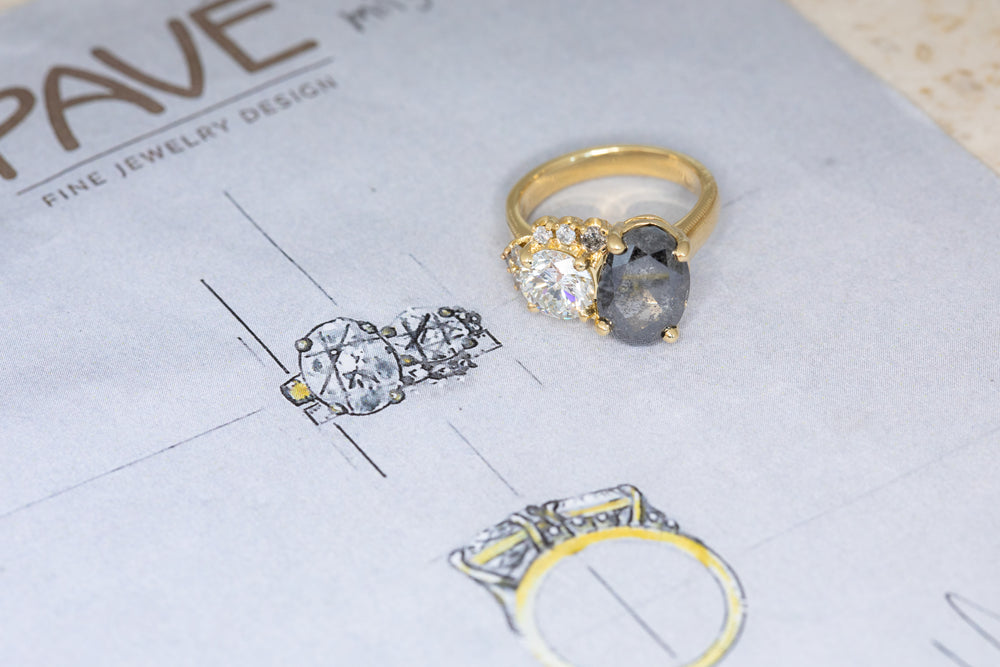 Gold and silver ring with gemstones on a jewelry design paper.