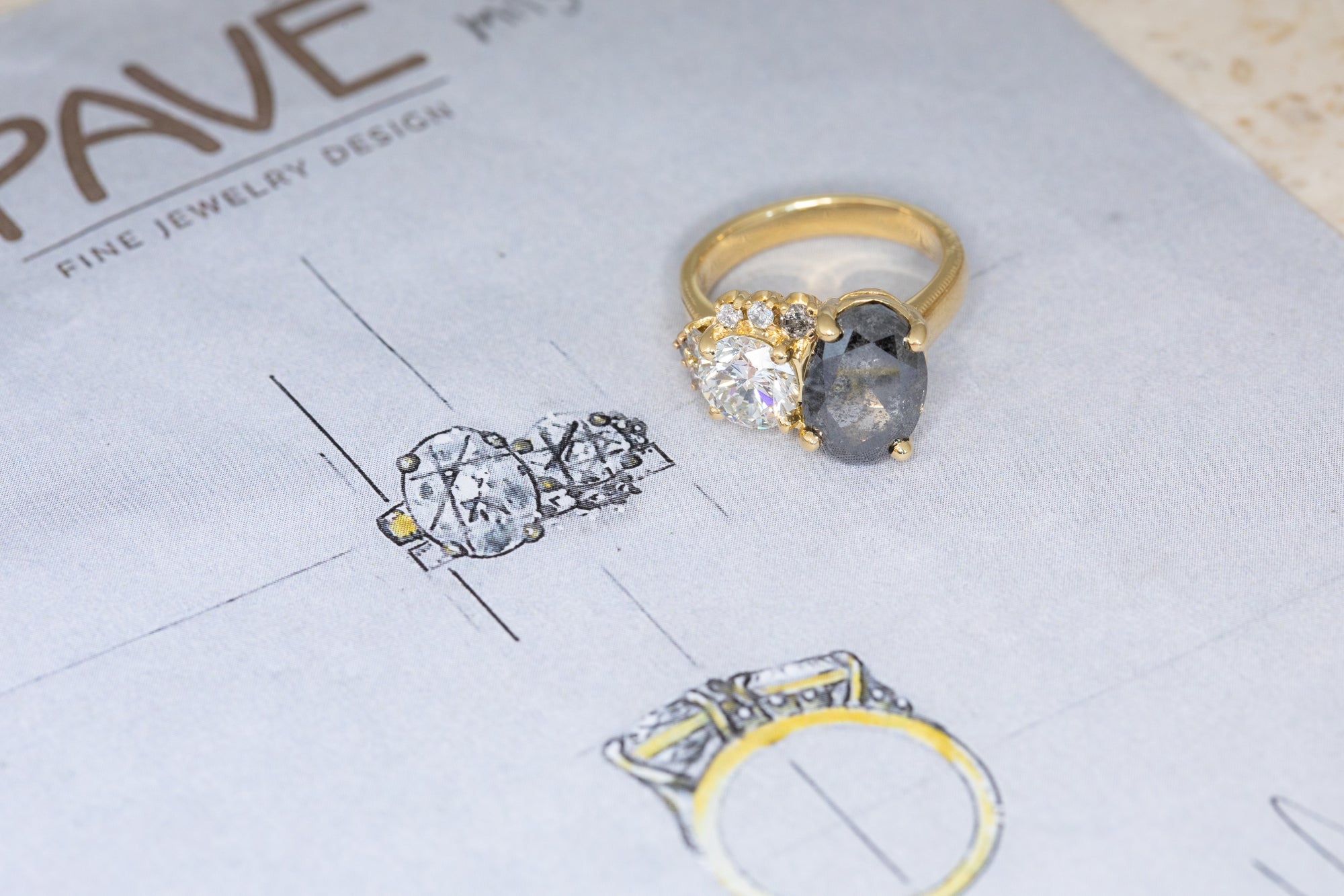 Gold and silver ring with gemstones on a jewelry design paper.