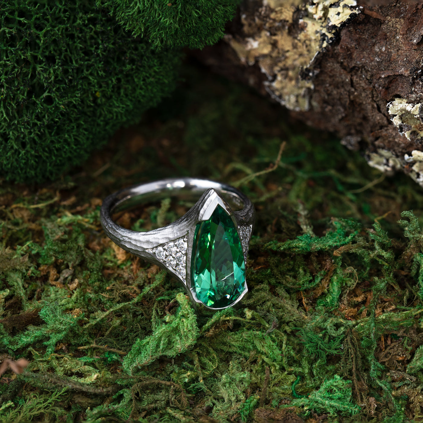 Platinum ring with a green gemstone on a mossy background