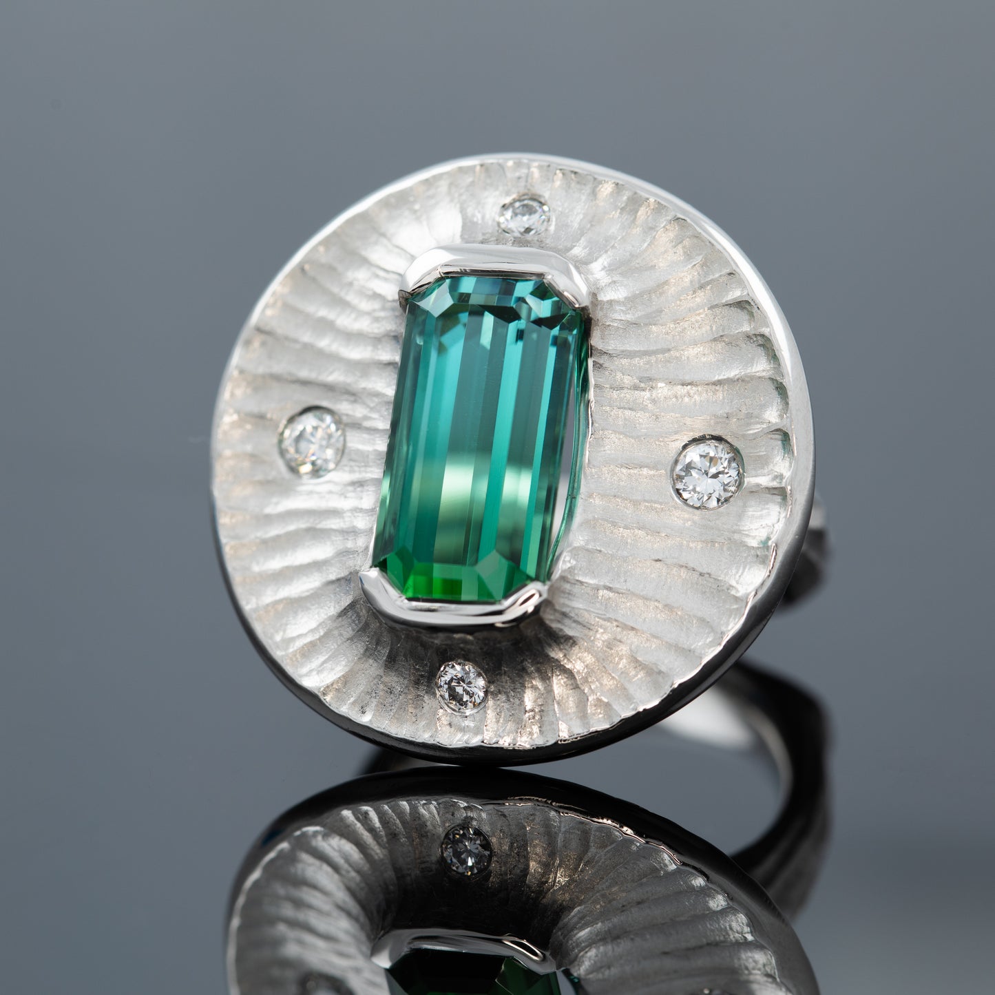 Platinum ring with a bicolor green gemstone on a dark grey reflective surface