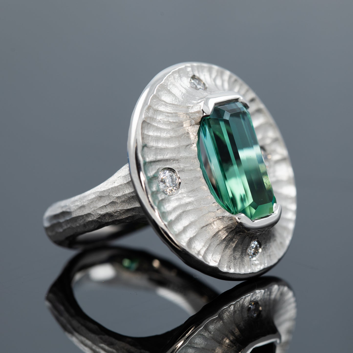 Platinum ring with a green gemstone on a dark grey reflective surface