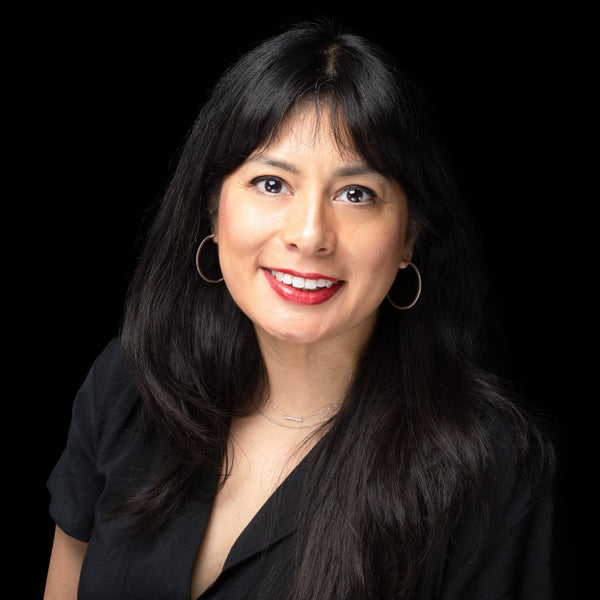 Woman with long dark hair wearing a black top against a black background