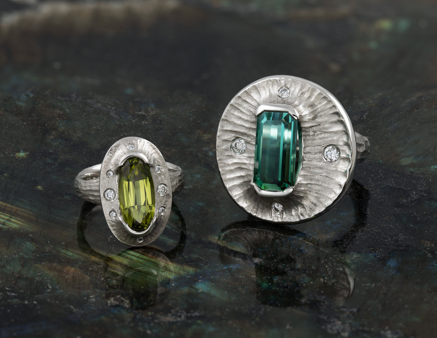 Two platinum rings with green gemstones on a dark textured surface