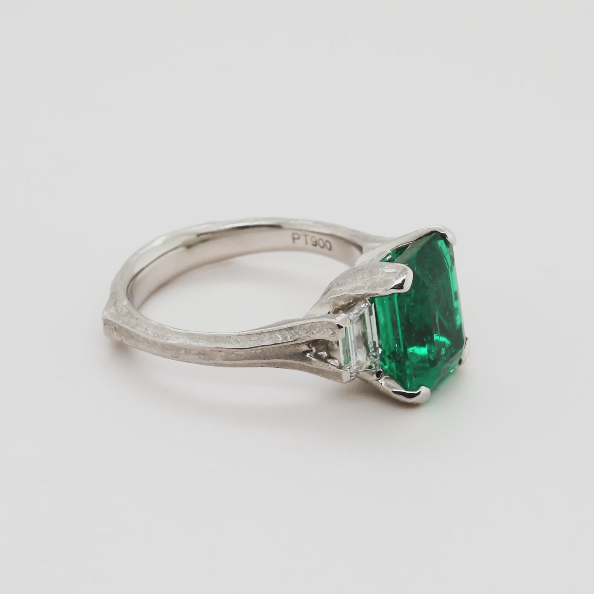 Emerald ring with side diamonds rotating 360 degrees on a white background