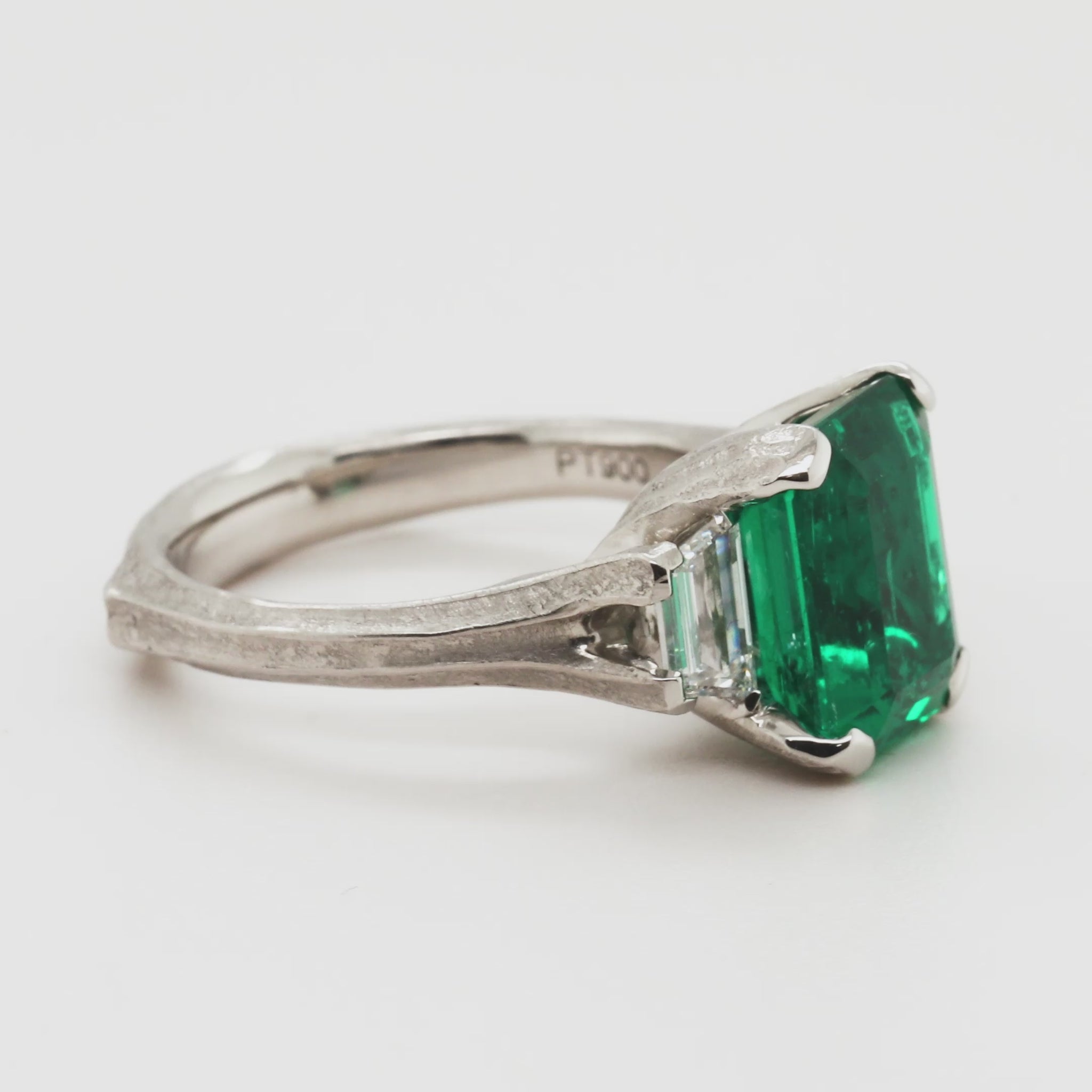 Emerald ring with side diamonds rotating 360 degrees on a white background