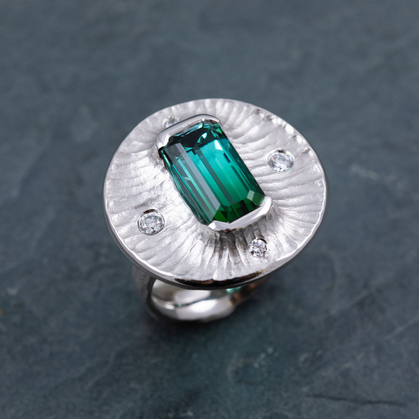 Platinum ring with a green gemstone on a dark gray stone background