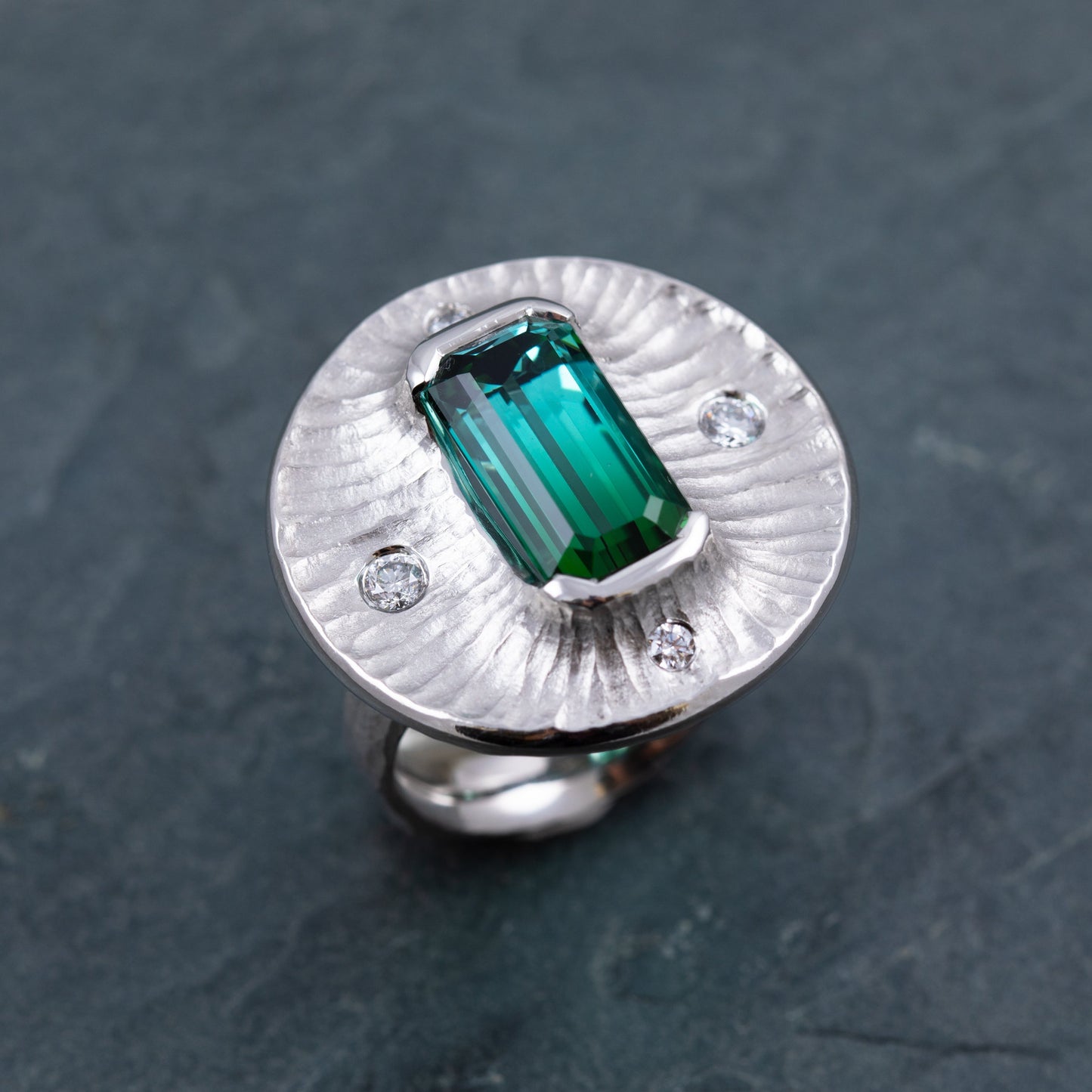 Platinum ring with a green gemstone on a dark gray stone background