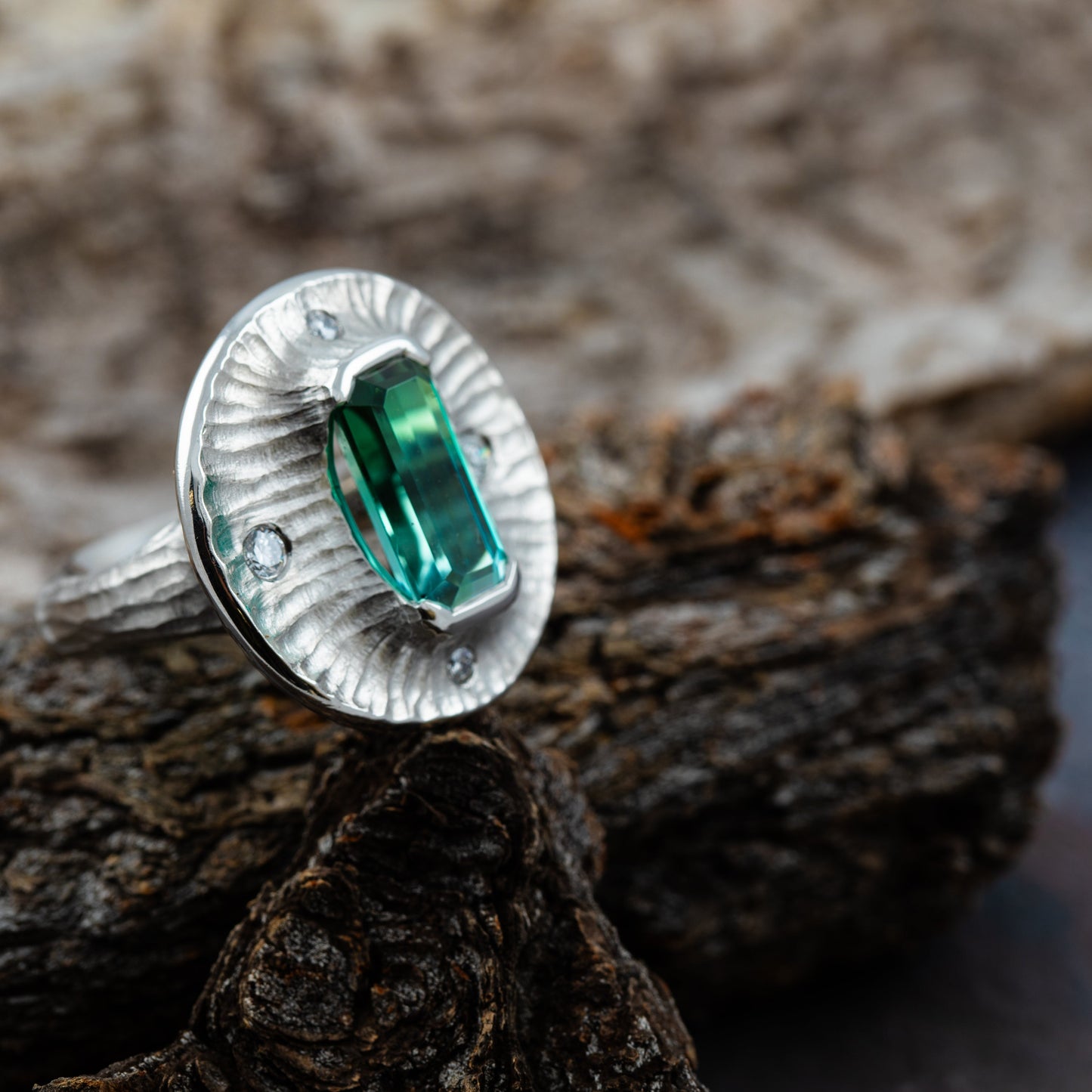 Platinum ring with a green gemstone on a wooden surface